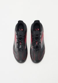 Black soccer shoes featuring red accents, sleek design, textured material, and a pointed toe shape. Laces extend through the upper for fit adjustment.