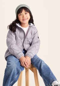 Gray quilted jacket with hood, featuring elastic cuffs and a front zipper. Paired with blue denim jeans and a light green ribbed beanie.