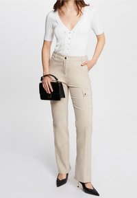 Biały prążkowany top z krótkim rękawem zdobiony guzikami, zestawiony z beżowymi spodniami cargo i czarną torebką. Czółenka na czarnym obcasie dopełniają stylizację.