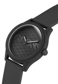 Reloj de pulsera redondo negro con esfera texturizada que muestra el logo repetido de "GUESS", texto grande "GUESS" y manecillas blancas de hora y minuto.
