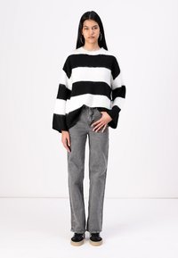 Black and white striped knit sweater with a relaxed fit, dropped shoulders, and wide sleeves. Paired with gray denim jeans and black shoes.