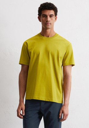 T-shirt à manches courtes, col rond en coton jaune-vert vif. Texture douce avec une coupe décontractée et un minimum de coutures au niveau de l'ourlet.