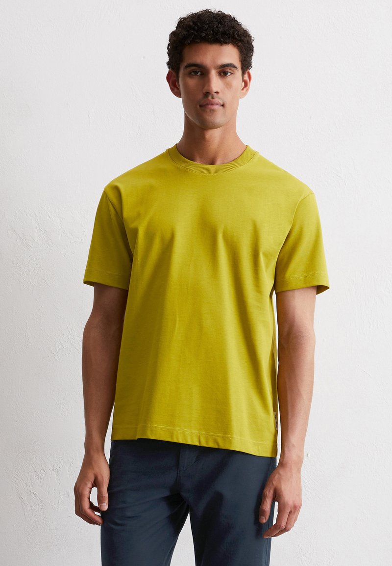 Koszulka z krótkim rękawem i okrągłym dekoltem w jaskrawym żółto-zielonym kolorze, wykonana z bawełny. Miękka w dotyku, o luźnym kroju i minimalnych detalach przeszyć u dołu.