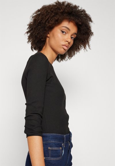 Top noir à manches longues côtelé avec un col rond, associé à un jean taille haute bleu foncé. Le tissu semble lisse avec une silhouette ajustée.
