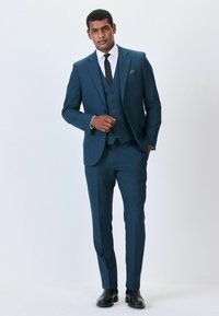 Zweiteiliges Anzugset aus dunkelblauem Stoff, bestehend aus einem Blazer mit Revers und passenden Hosen. Komplett mit einem weißen Hemd und einer schwarzen Krawatte.