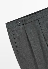 Pantaloni grigi in misto lana con fronte piatto, due tasche laterali e chiusura con bottone. Presentano un tessuto testurizzato e pieghe angolate.