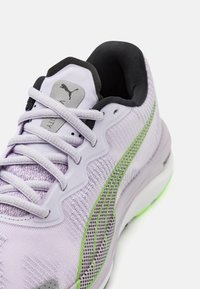 Baskets de sport lilas clair avec empeigne en mesh, accents verts et languette rembourrée. Comprend des lacets plats, une semelle en caoutchouc et un détail texturé sur le côté.