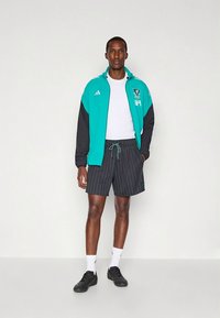 Sportjasje in teal en zwart, wit T-shirt, shorts met krijtstreep en zwarte sneakers met witte sokken. Voorzien van logo's en trekkoord.