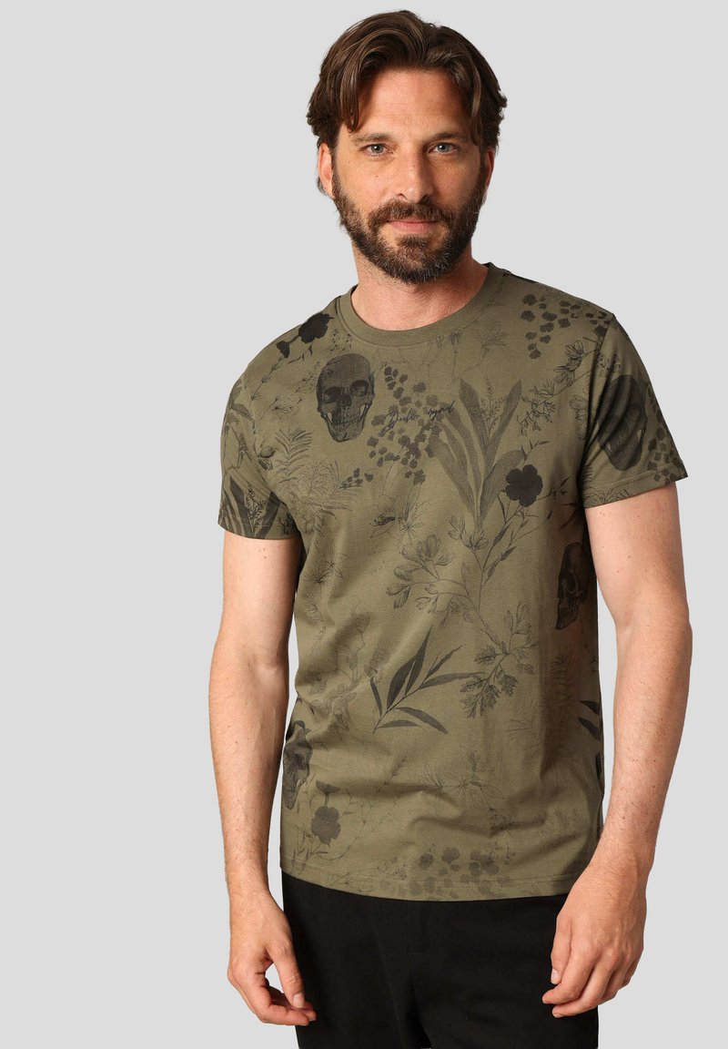 T-shirt en coton vert olive avec un imprimé floral et crâne en gris foncé. Manches courtes, col rond et coupe décontractée. Dos uni.