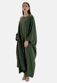 Vestito lungo e morbido in tessuto verde scuro, con maniche ampie e scollo arrotondato. Caratterizzato da dettagli drappeggiati e una superficie liscia.