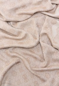 Μπεζ ύφασμα με διακριτικά υφασμένα λουλουδάτα σχέδια και γεωμετρικές γραμμές, απαλά διπλωμένο για να αναδείξει τις υφαντές λεπτομέρειες και την υφή.