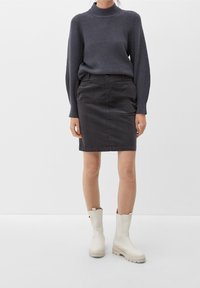 Pull à côtes gris, jupe en tissu gris foncé, et bottines crème avec surface texturée et détails subtils contrastants.
