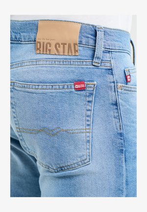 Jasnoniebieskie dżinsy z denimu z skórzaną naszywką z napisem "BIG STAR" na pasku i czerwonymi metkami z logo na tylnych kieszeniach.