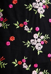 Tecido preto com bordados florais coloridos em rosa, vermelho e verde, com detalhes intrincados e diferentes formas e tamanhos de flores.