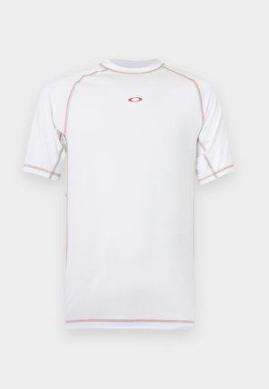 T-shirt de sport blanc à manches courtes avec des détails de couture rouges et un petit logo ovale rouge centré sur la poitrine, présenté sur un fond uni.
