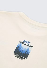 Helles T-Shirt in Creme mit einem rechteckigen Grafikdesign, das eine Silhouette der Skyline in Blautönen zeigt, sowie dem Text: "NYC HAVE NO PLAN" und "Die besten Sachen geschehen unerwartet."