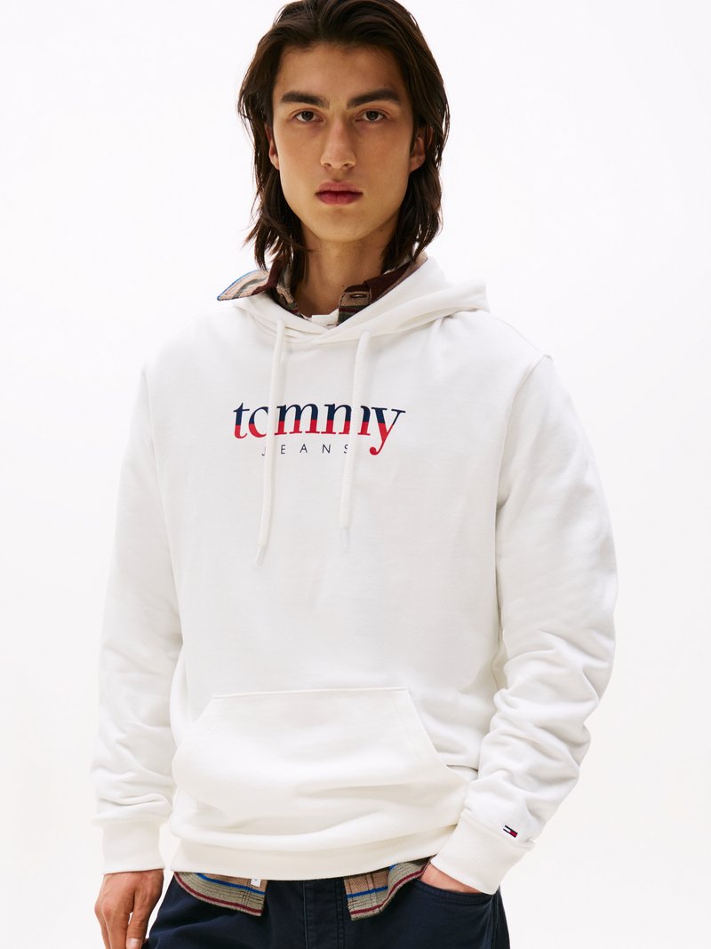 Sudadera blanca con el logo de "tommy jeans" en azul marino y rojo. Tela suave, capucha con cordón, bolsillo frontal, puños acanalados, superpuesta a una camisa de cuadros.