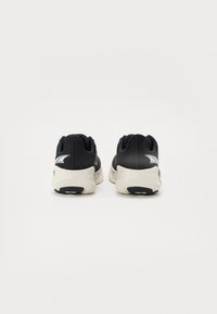 Black athletic shoes with a textured upper, white midsole, and rubber outsole featuring a zigzag pattern; reflective accents on the heel.