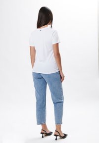 Hvid crew-neck t-shirt med korte ærmer, parret med lyseblå lige ben jeans og sorte hælede sandaler. Synlig detalje på ryggen ved kraven.