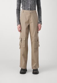 Kargo kalhoty ve světlém bavlněném materiálu, vybavené několika postranními kapsami, přímým střihem a pohodlným střihem. Nosí se s šedým tričkem s dlouhým rukávem.