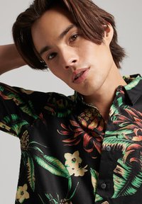 Camicia nera a maniche corte con un vivace motivo tropicale di fiori e foglie nei colori verde, giallo e rosso; design aderente con colletto e bottoni.