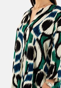 Túnica multicolor en un patrón abstracto de verde, negro y azul con escote en V y mangas sueltas; tejido texturizado con una caída fluida.