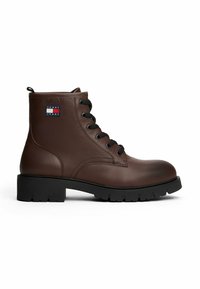 Braune Leder-Ankelstiefel mit schwarzer Gummisohle, runder Spitze und sechs Ösen. Logopatch an der Außenseite. Schnürsenkel und Obermaterial aus strukturiertem Leder.