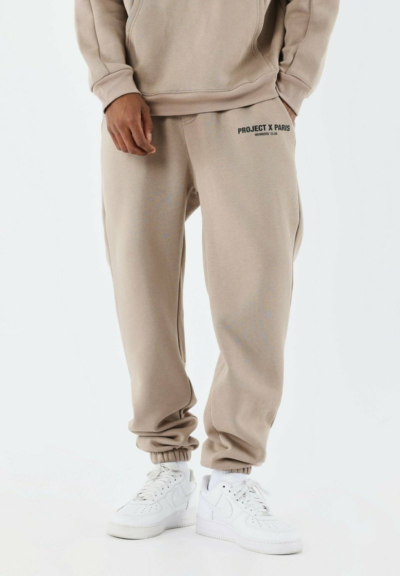 Joggers beige hechos de una suave mezcla de algodón, con cinturilla y puños elásticos. Logo "PROJECT X PARIS" en la cadera izquierda. Combinados con zapatillas blancas.