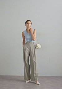 Light blue ribbed sleeveless top with lace-up detail, paired with gray high-waisted pleated trousers and white pointed-toe heels. White bag.