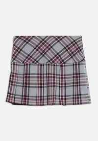 Jupe plissée grise avec un motif à carreaux noir, blanc et bordeaux, soigneusement pliée sur un fond blanc.
