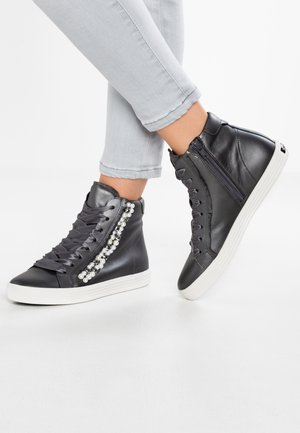 Black high-top sneakers with white soles, pearl and bead embellishments, side zipper, worn with light grey rolled-up jeans.