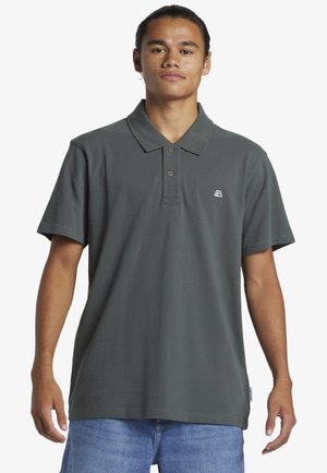 Mørkegrøn polo-shirt med klassisk krave, korte ærmer og et lille logo på venstre bryst. Stof ser blødt og glat ud.