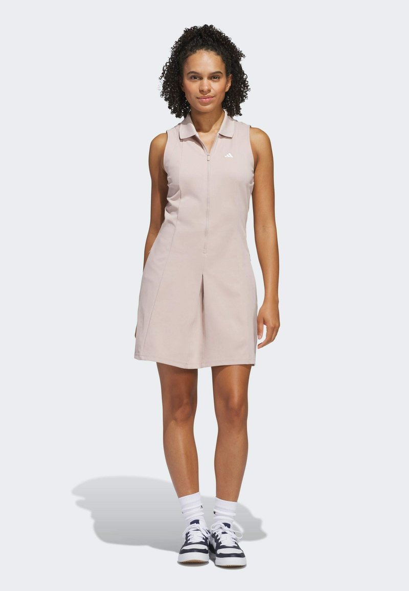 Vaaleanpunainen hihaton mekko, jossa on vetskari, kaulus ja laskostettu hame. Yhdistetty valkoisiin korkeisiin sukkiin ja tummansinisillä raitakenkiin.