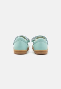 Chaussures en cuir bleu clair avec un dos arrondi, semelles en caoutchouc beige et bandes velcro. Texture lisse avec des détails de design discrets au niveau du talon.
