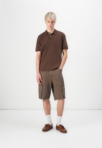 Brown polo shirt with a classic collar, paired with brown cargo shorts featuring side pockets. Brown shoes and white socks complete the outfit.