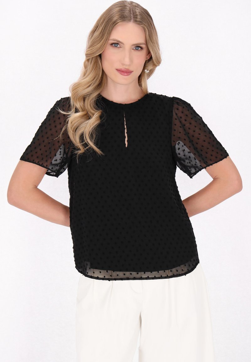 Sort gennemsigtig bluse med teksturerede polka dots, korte pufærmer, en nøglehulsudskæring og en bølget kant.