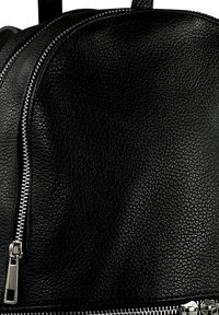 Sac à dos en simili cuir noir de forme arrondie, avec une finition texturée, des fermetures éclair argentées et des bretelles doubles pour un transport facile.