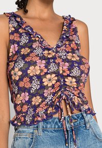 Květinový crop top v purpurové a růžové barvě s volánkovým výstřihem a nařaseným předním dílem. Vyrobený z lehkého materiálu, má kravatu na spodním lemu.