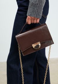 Braune Kunstleder-Handtasche mit einem goldfarbenen Verschluss und einer Kettenriemen, rechteckige Form, mit einer glatten Textur und minimalistischen Design.