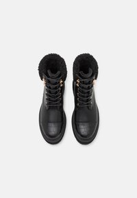 Stivali neri in pelle fino alla caviglia con fodera in pelliccia sintetica, punta texturizzata effetto coccodrillo e occhielli metallici per i lacci. Punta rotonda e collo imbottito.