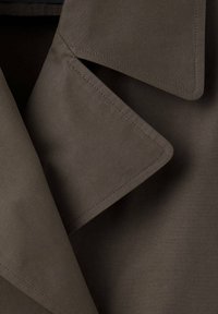 Gros plan de sections de tissu marron superposées avec des plis triangulaires nets et cousus formant des formes géométriques propres.