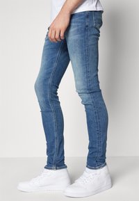 Blå skinny jeans med en urtvättad struktur, med en klassisk femfickdesign. Parat med vita hög-top sneakers.