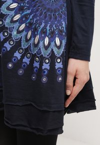 Robe bleu marine présentant un motif circulaire multicolore avec des paillettes à l'ourlet. Tissu doux avec un design fluide et des détails en couches.