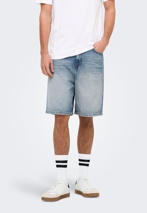 Lette blå denimshorts i en afslappet pasform med en rå kant. Kombineret med hvide sneakers og sorte og hvide stribede sokker.