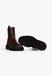 Botas de tobillo de cuero marrón con suela de goma negra gruesa y un ligero tacón, con paneles laterales elásticos y una lengüeta.