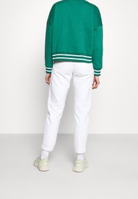 Sudadera verde con puños y dobladillo a rayas blancas, combinada con pantalones blancos entallados y zapatillas ligeras. Tejido texturizado, ajuste informal.