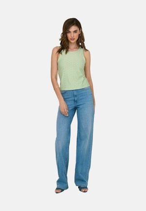 Lichtgroene mouwloze top met een gestructureerd ontwerp; gecombineerd met hoge taille blauwe jeans en zwarte open teen hakken.