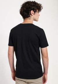 Camiseta negra de manga corta hecha de algodón con un diseño clásico de cuello redondo. La parte posterior presenta una textura suave y detalles de costura mínimos.