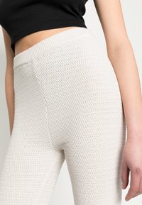 Leggings de malha bege claro com superfície texturizada, cintura elástica e design sem costuras. O material parece elástico e respirável.