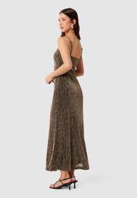 Robe maxi en tissu métallisé or et bronze, avec un corsage ajusté, des fines bretelles et une jupe évasée, associée à des sandales à talons noires.